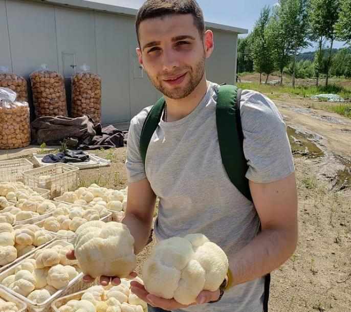 Мужчина держит гриб на руках на фоне фермы